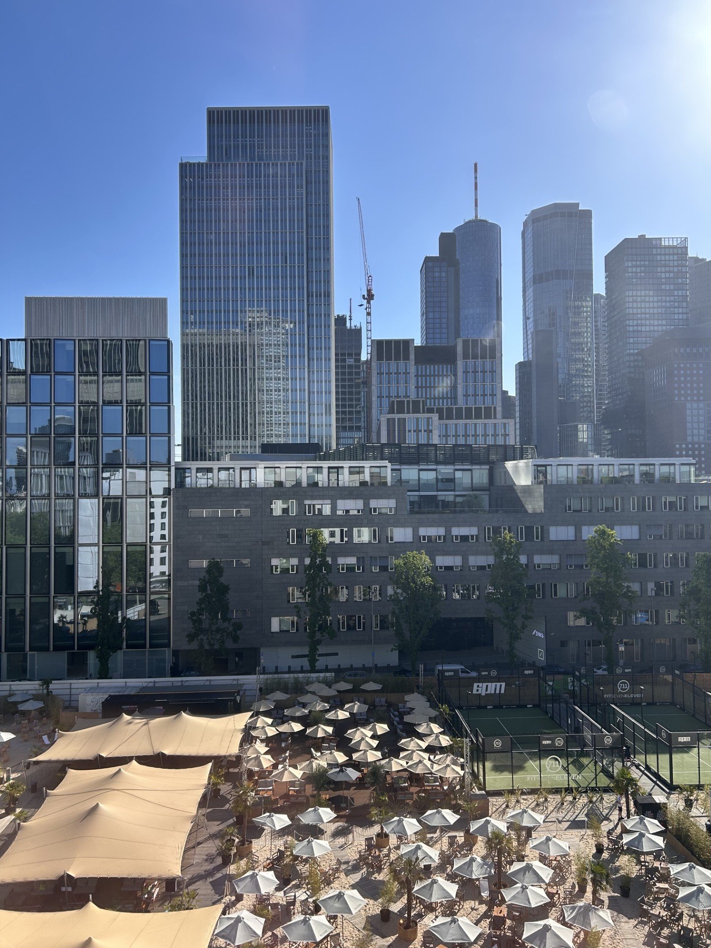 City skyline with tall modern buildings and construction cranes, seen from outdoor patio with umbrellas and tables. Overlooking the Gibson Beach Club, this is the views from the hotel's guest rooms.