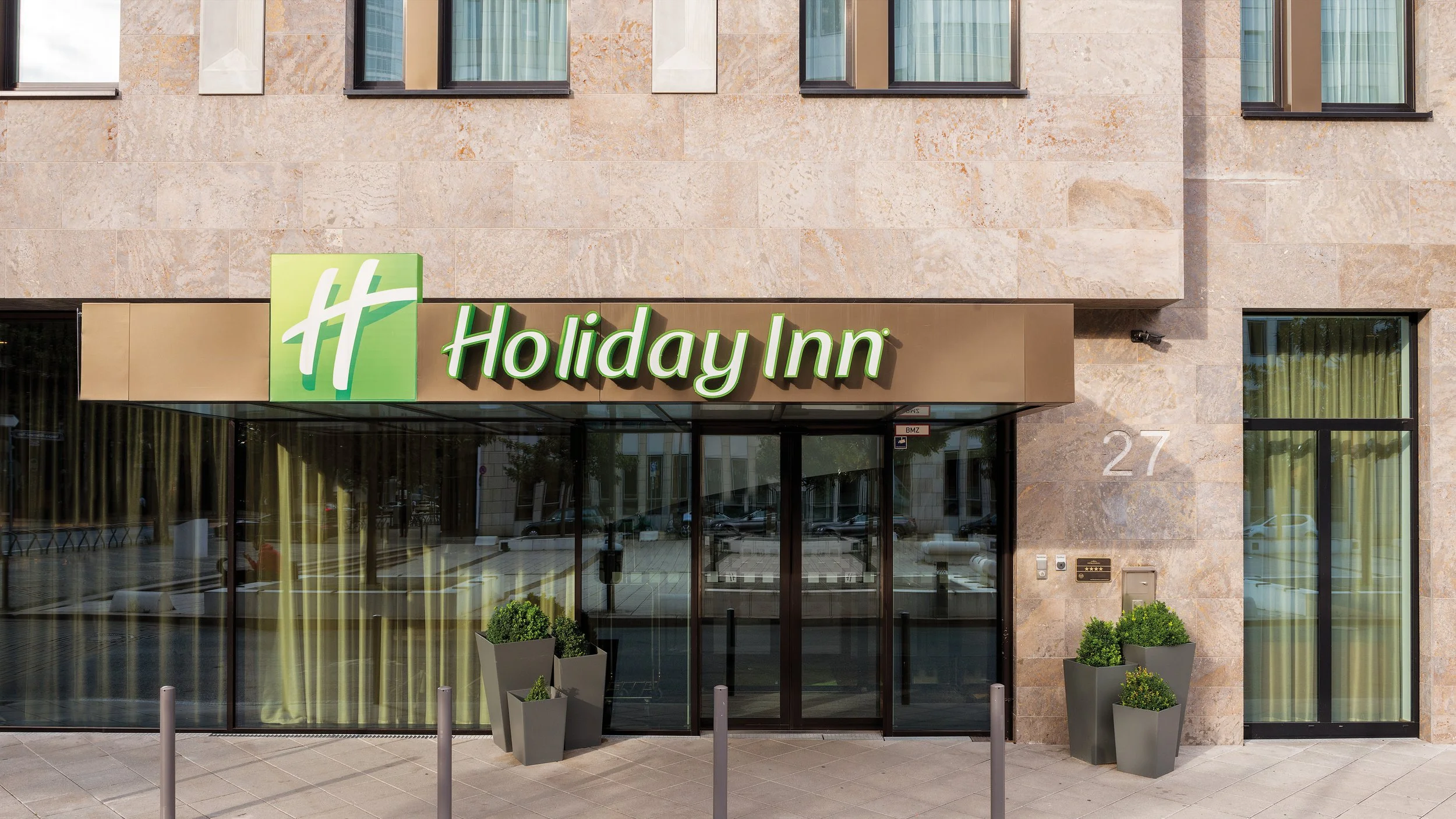 The exterior of a Holiday Inn hotel with a sign above the entrance, glass doors, and potted plants in front. Holiday Inn Frankfurt - Alte Oper is the number 1 property on TripAdvisor.