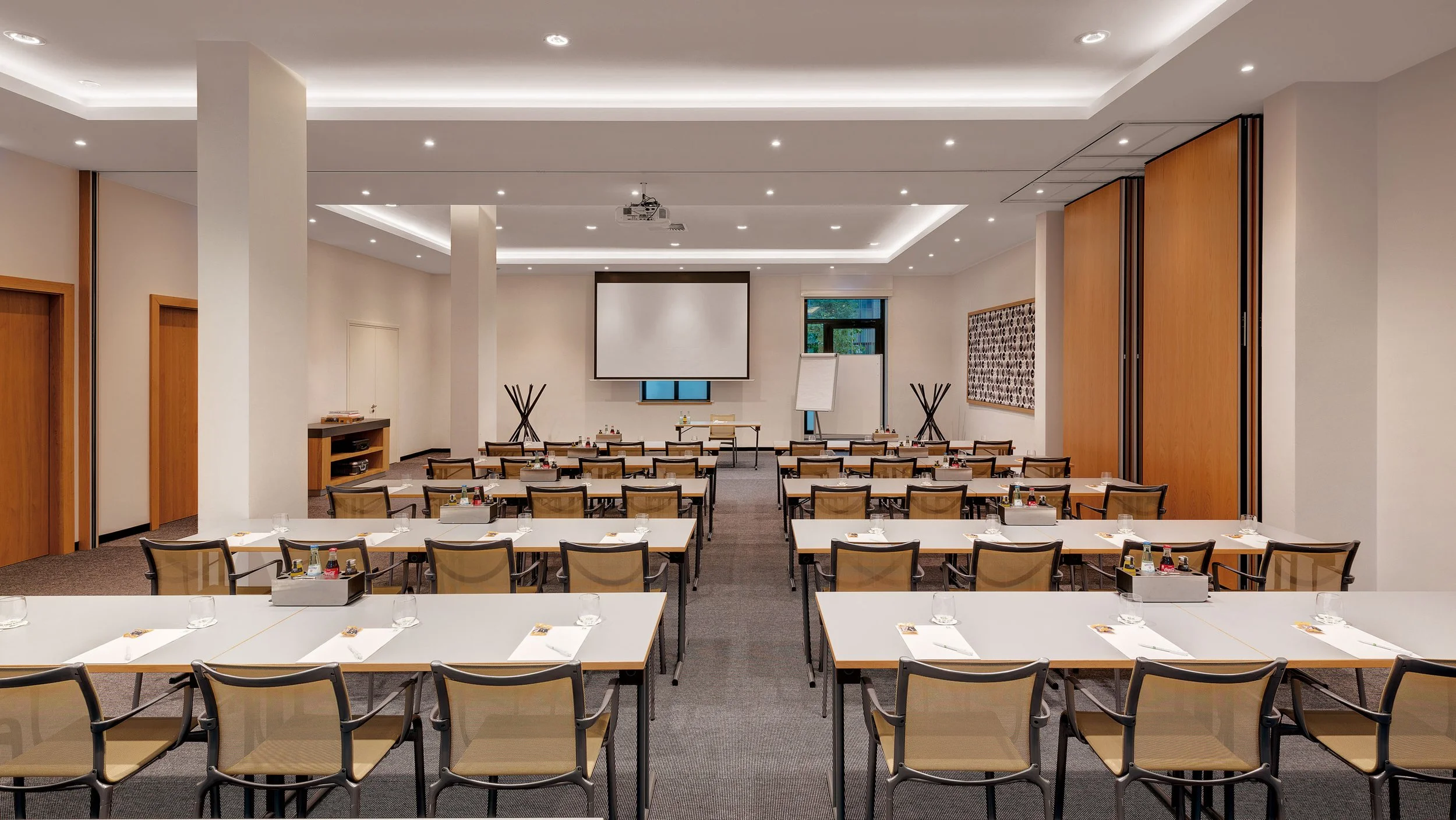 Empty conference room with chairs arranged in rows facing a large projection screen and whiteboard, set up for a meeting or seminar.