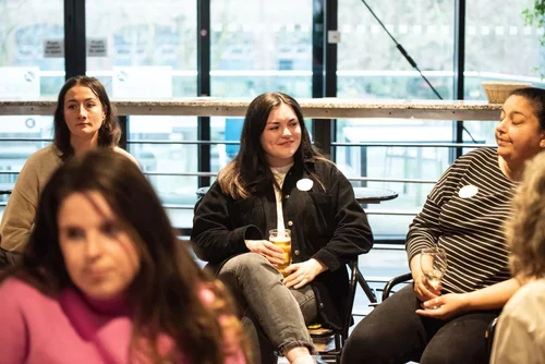 Group of women sitting and chatting in a modern indoor space with large windows.