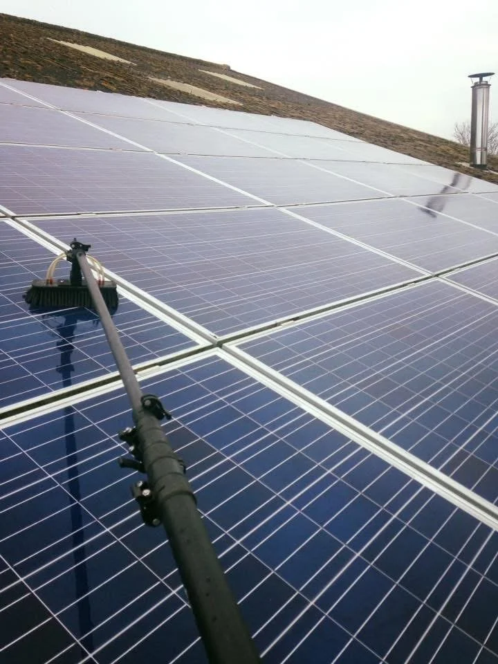 A person cleaning solar panels on a roof with a long-handled brush.