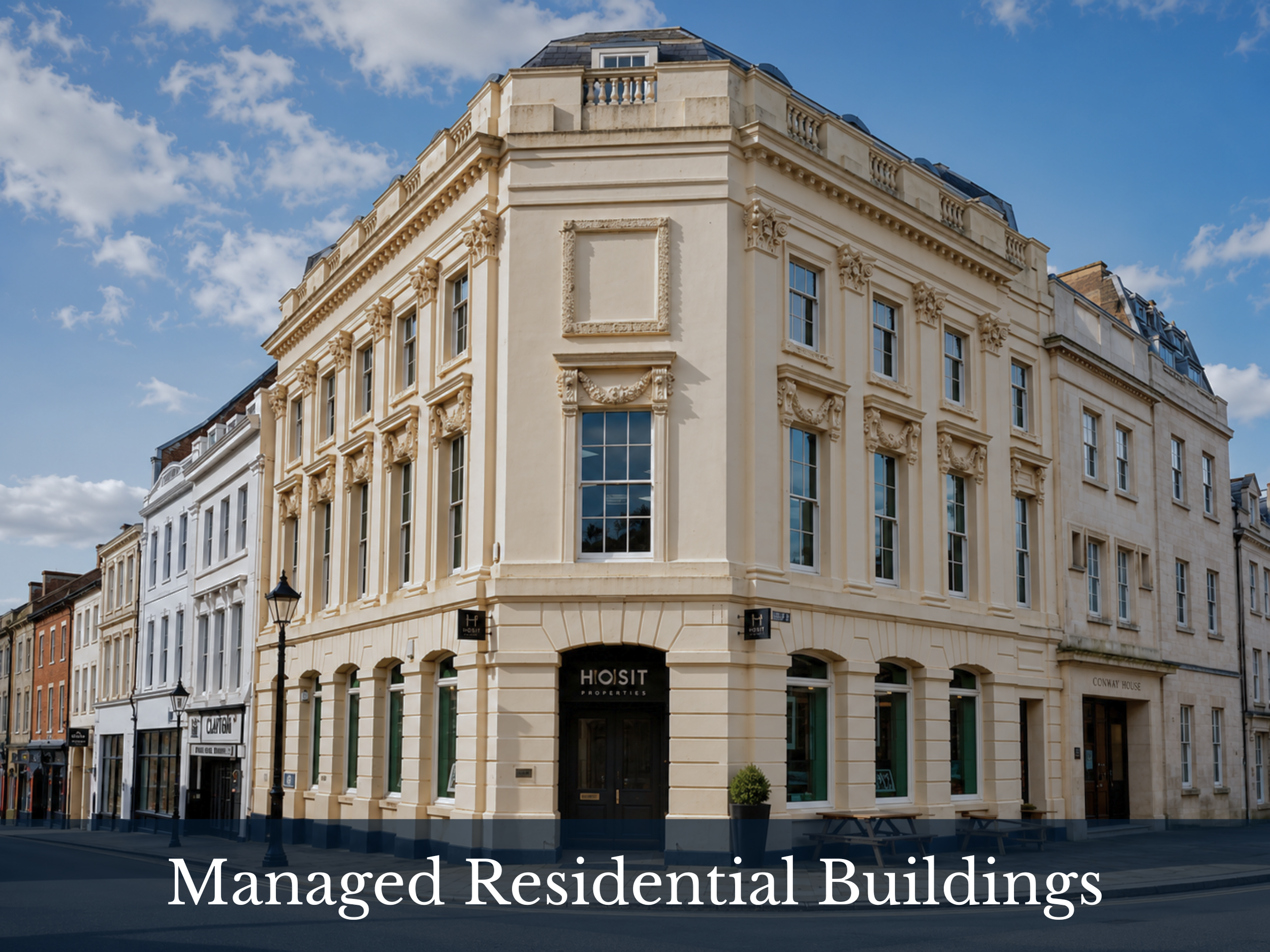 A cream-colored classical style building with decorative architectural details on a city street, under a blue sky with some clouds.