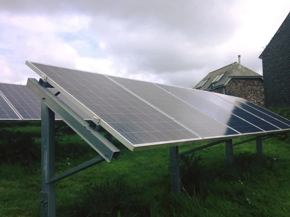 Solar panels installed on a grassy hill with cloudy sky and houses in the background.