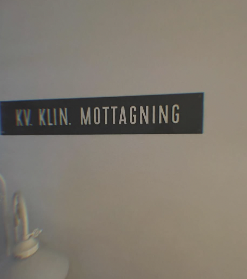 Texten "KV. KLUN. MOTTAGNING" på en svart etikett på en beige vägg, delvis synligt vardera
