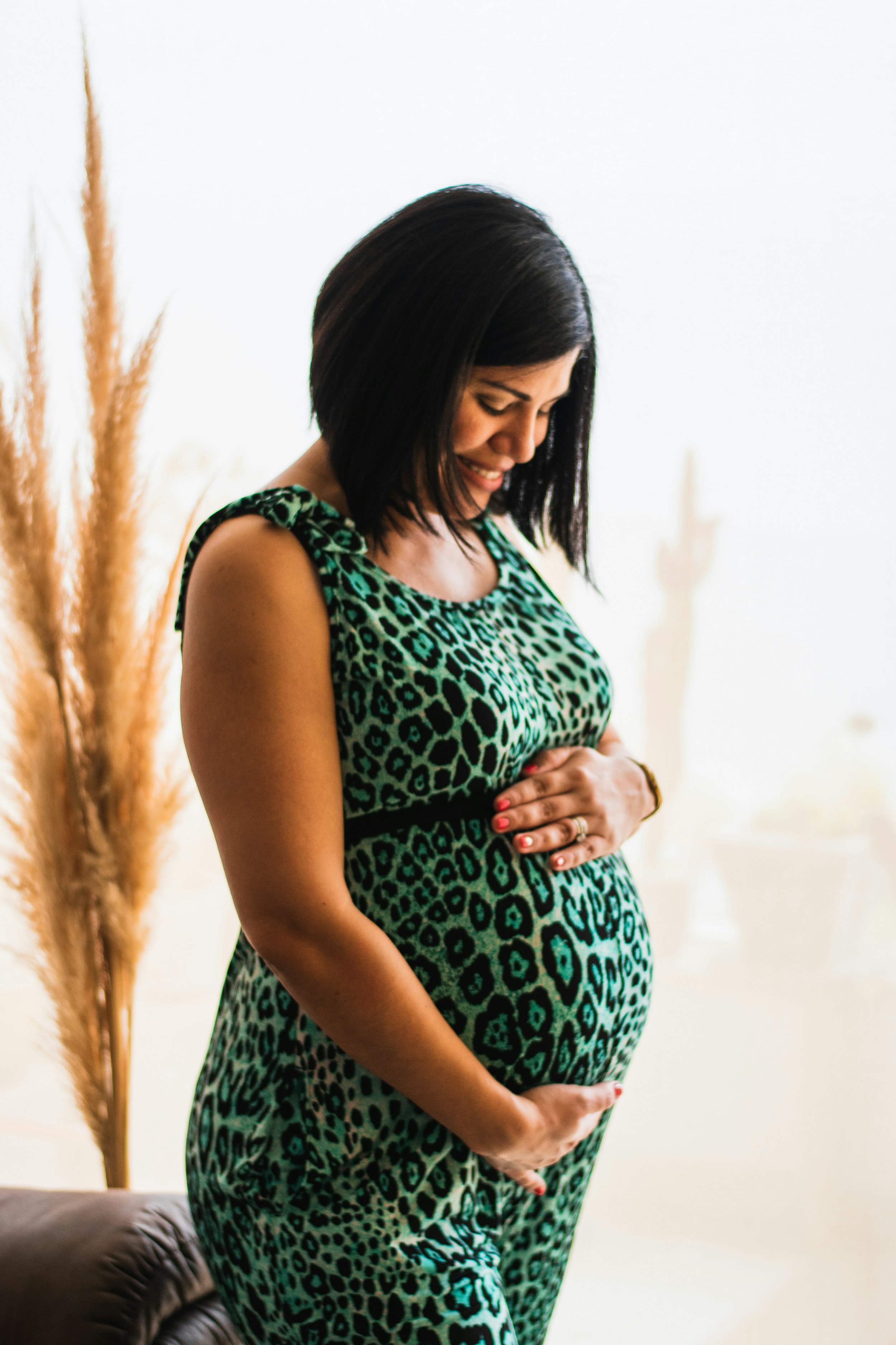 a woman with short hair, wearing a dress, is smiling holding her pregnant belly