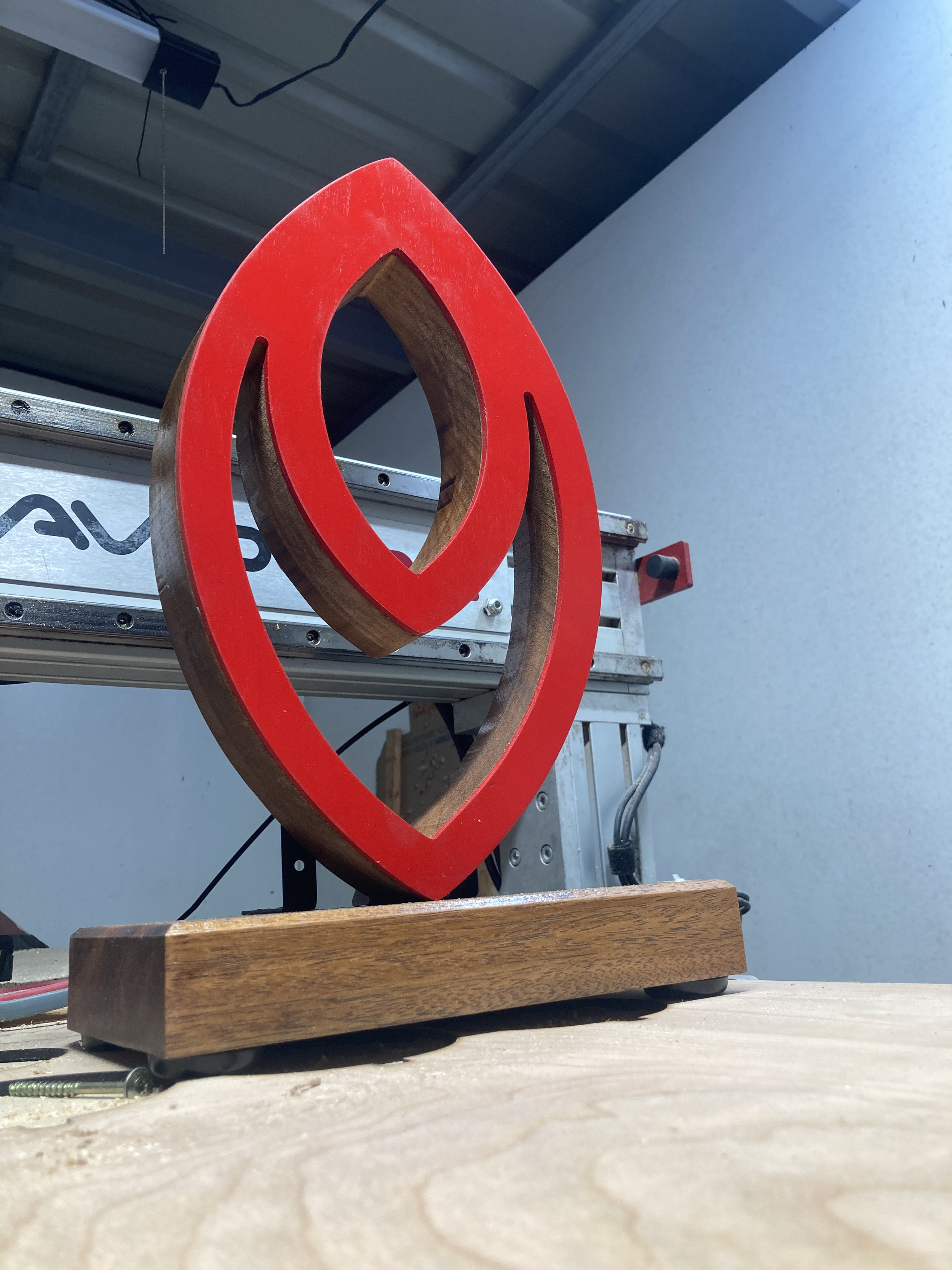 A wooden and red heart-shaped object mounted on a metal frame, placed on a wooden surface in a workshop setting.