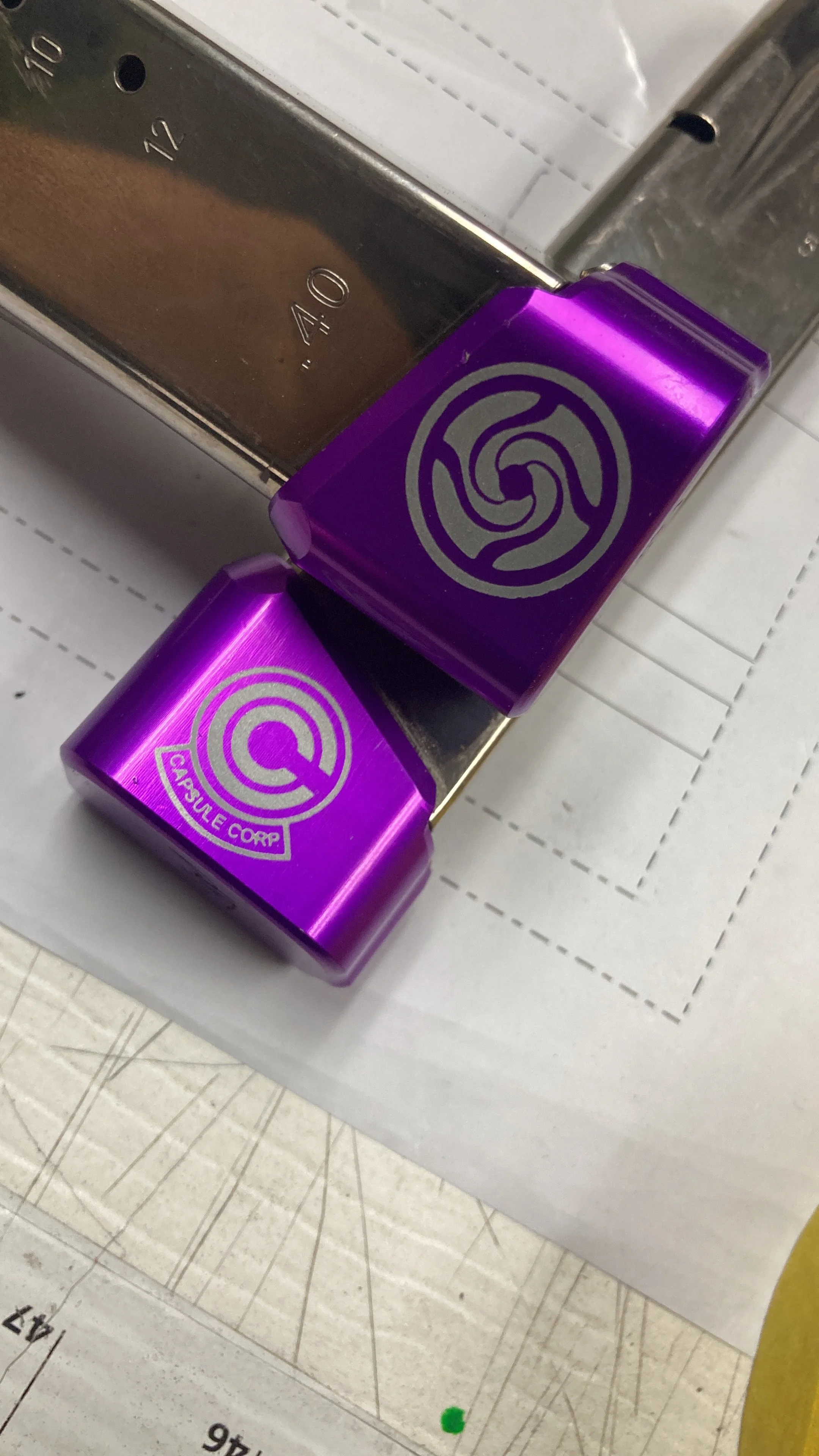 Close-up of a purple object with a logo, placed on a metallic surface and a sheet of paper with lines and measurements underneath.