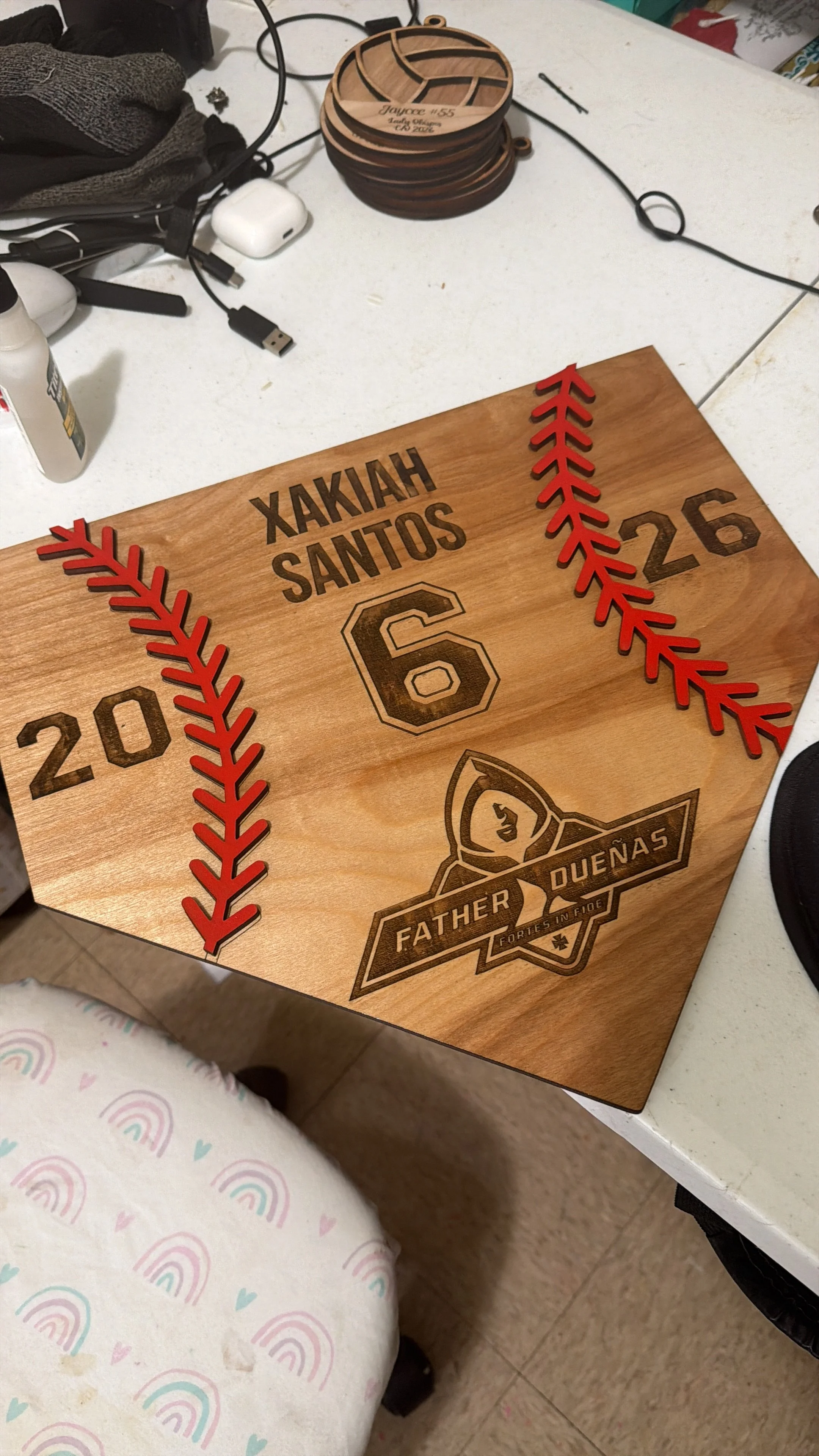 A wooden plaque with engraved text and logos, featuring red decorative elements resembling baseball stitching, and the name 'Hakhiah Santos' along with the number '26'.