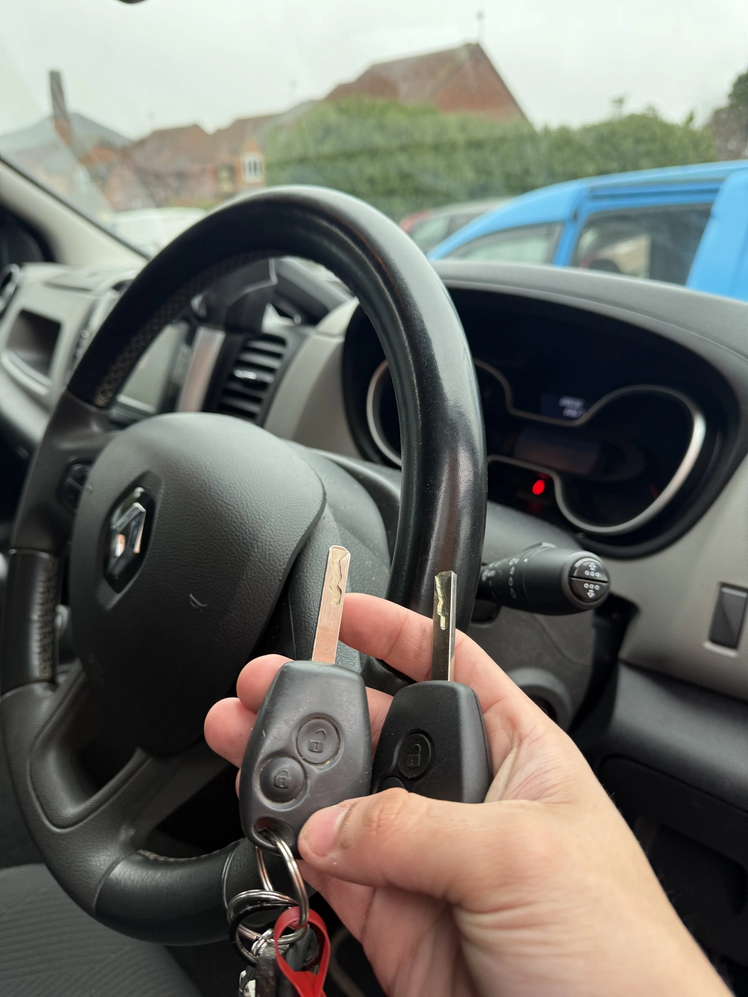 A person holding three car keys inside a car, with the steering wheel and dashboard visible in the background.