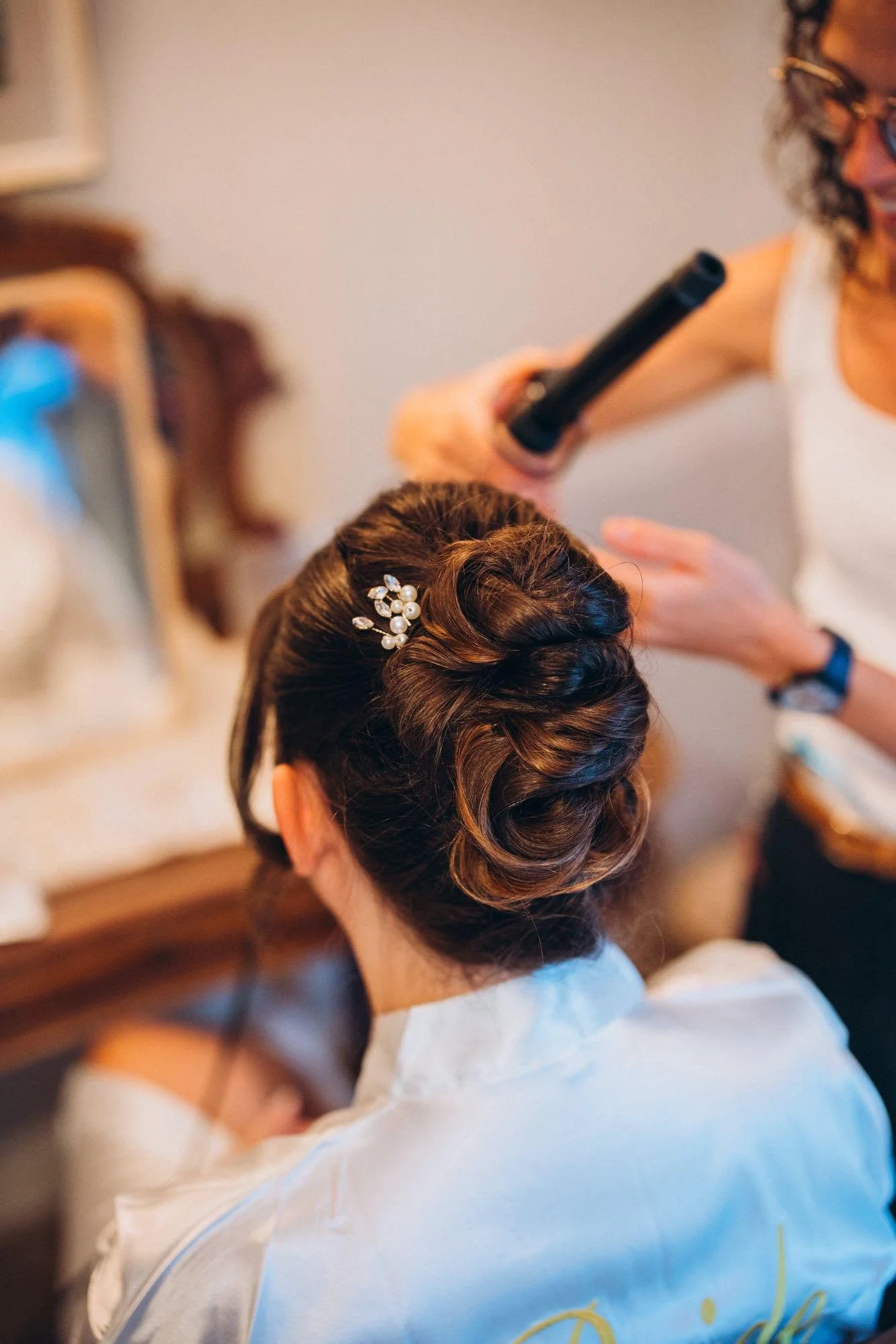 Une femme coiffant une femme dont les cheveux sont élégamment bouclés avec une barrette perles.