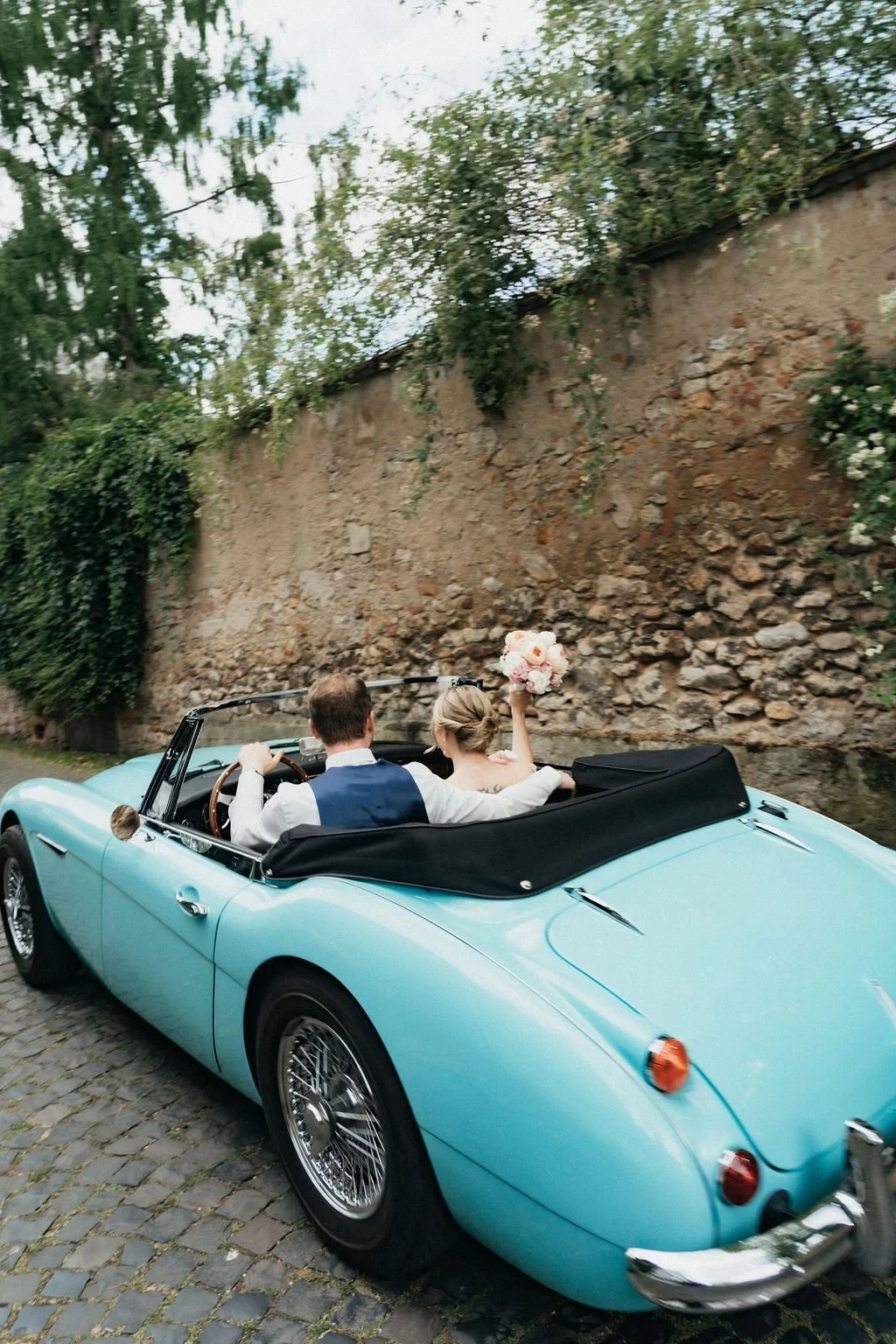 Groom and bride captured driving by in a classic car by photographer Jessica Di Salvo.
