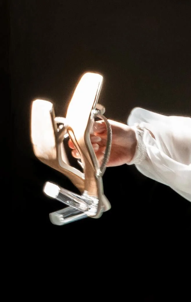 Person holding clear high-heeled shoes against a black background.