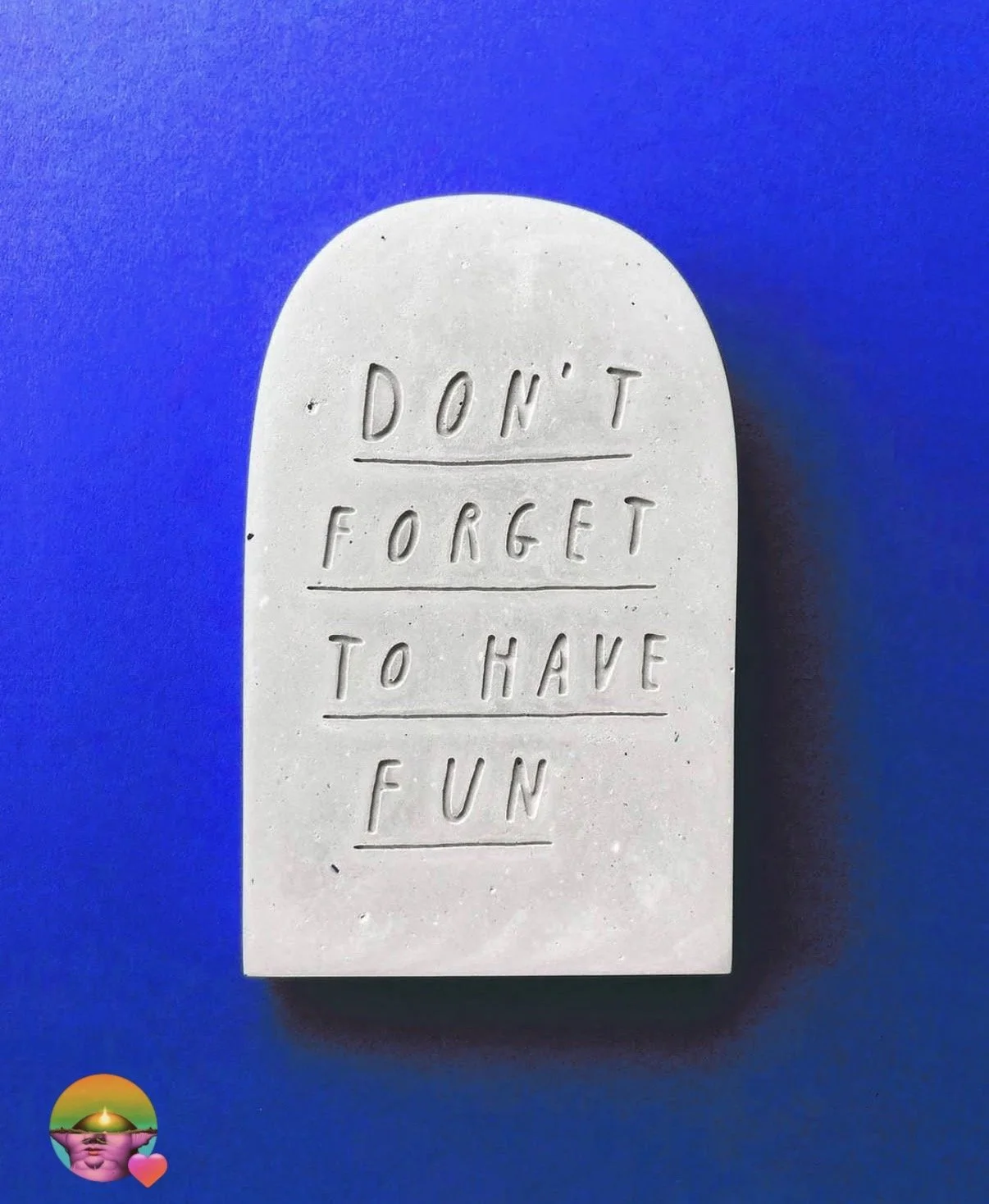 Una piedra gris con la inscripción 'Don't forget to have fun' en letras grabadas, sobre un fondo azul.