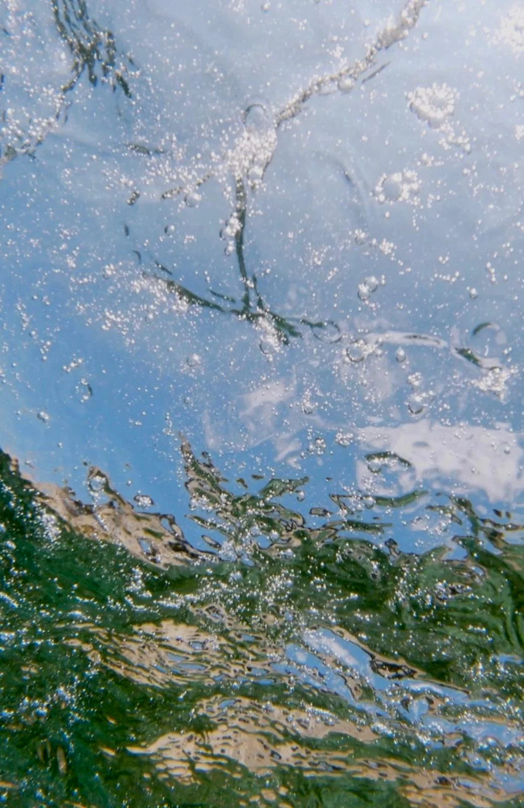 Close-up of water reflecting the sky with bubbles and ripples.