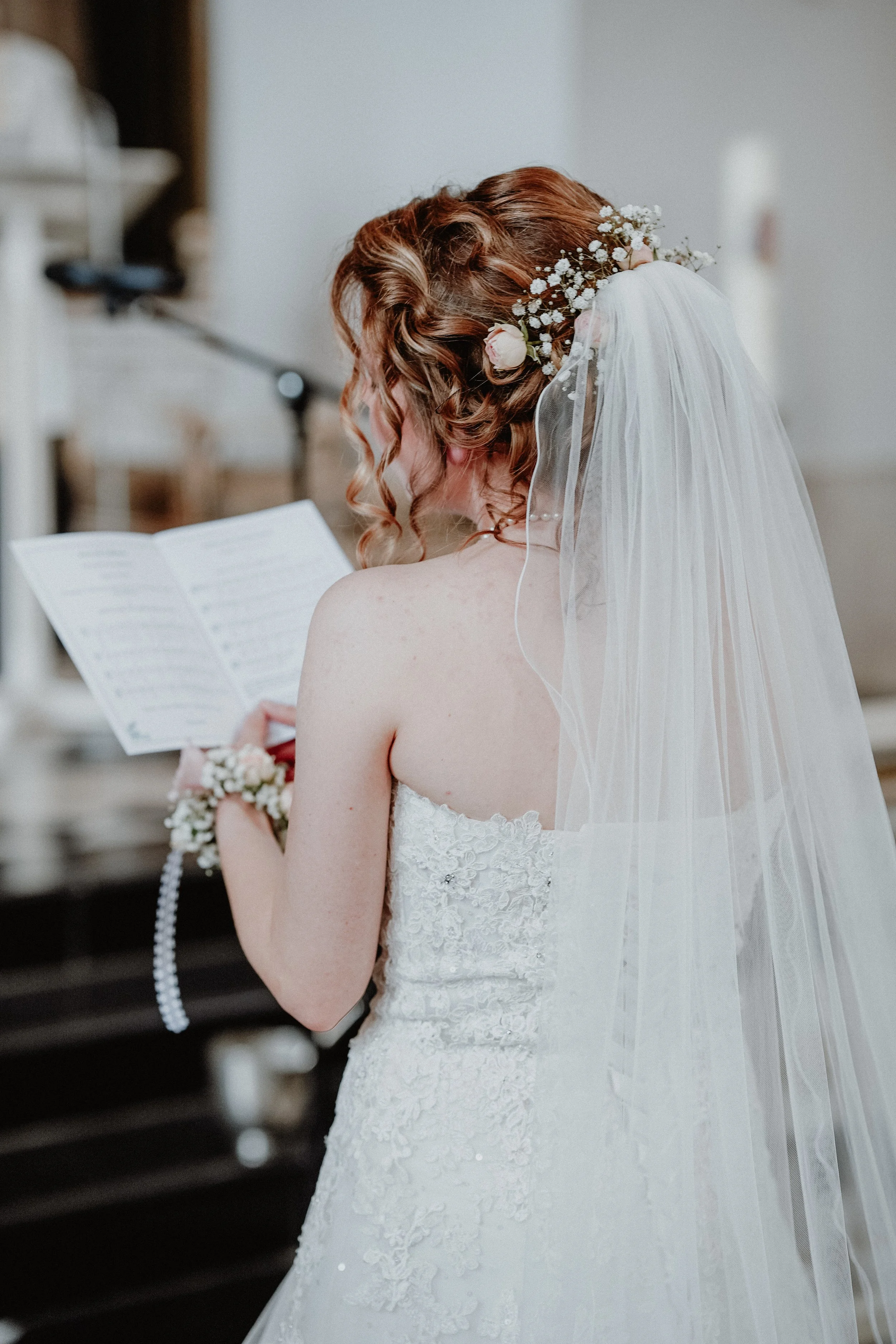 Braut in weißem Hochzeitskleid mit Bolero, Hochzeitsblumen im Haar, zitiert beim Lesen einer Rede, an einer Kirche.