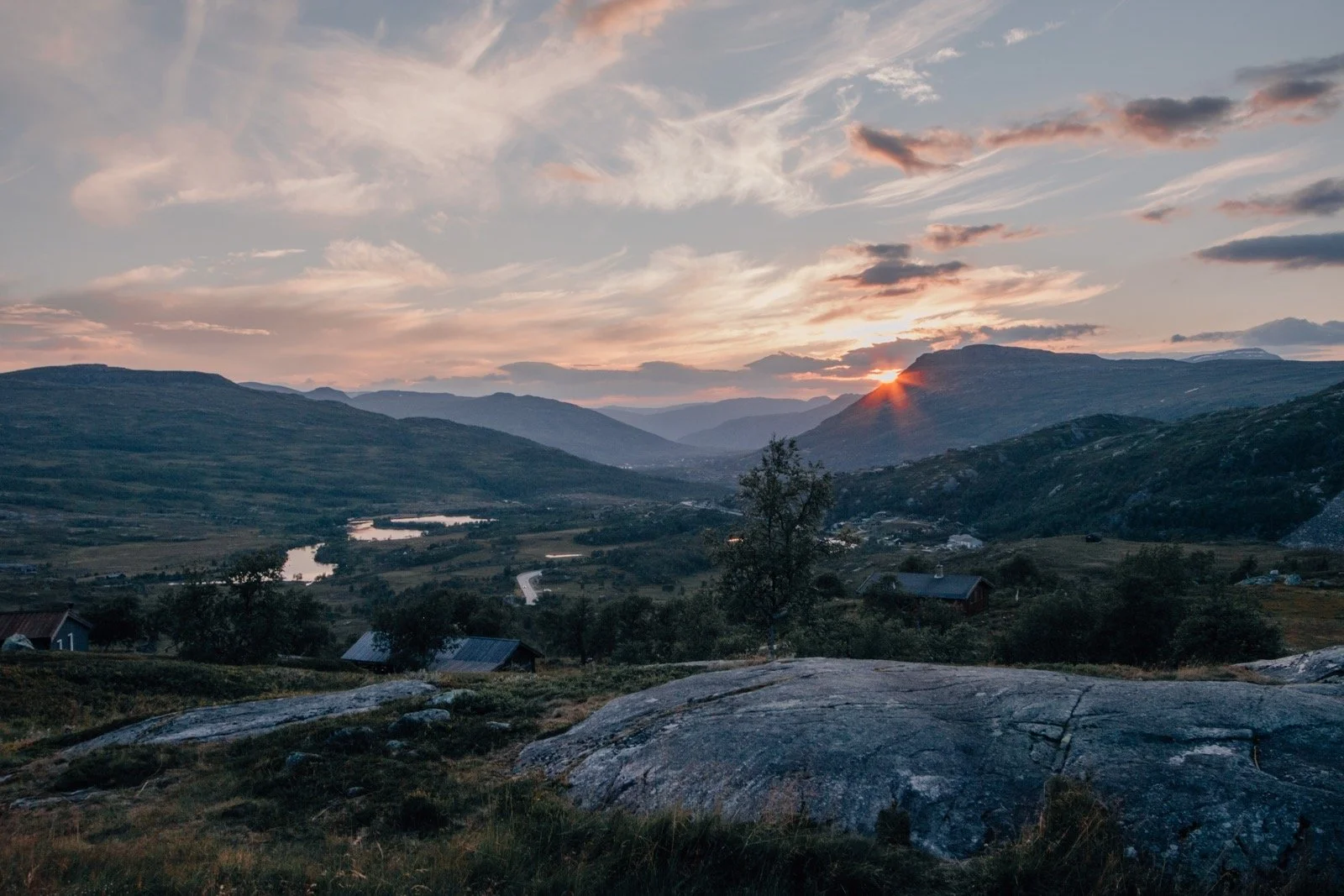 Berglandschaft bei Sonnenuntergang mit Wolken, Flüssen und kleinen Häusern