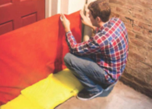 A person squatting and measuring or fixing a red upholstered chair or sofa in a room with exposed brick wall.