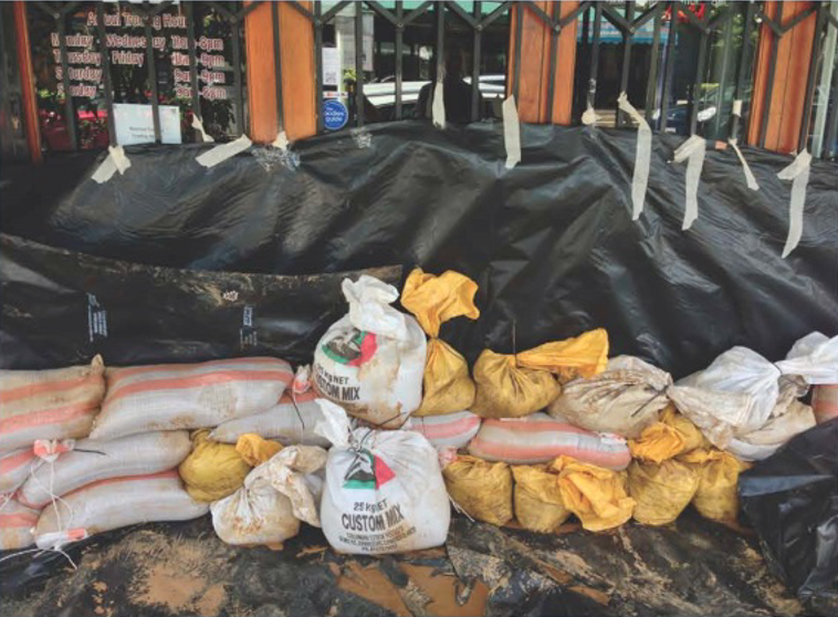 Sandbags and black plastic barriers stacked outside a building, possibly for flood protection.