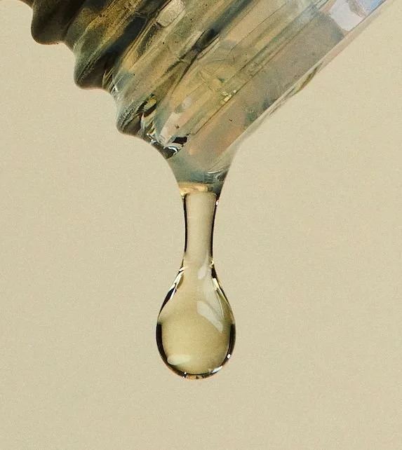 Close-up of a glass dropper with a clear liquid forming a single droplet about to fall.