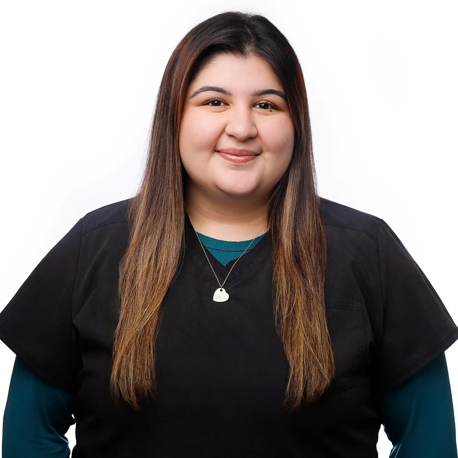 A young woman with long dark brown hair, smiling, wearing a black top with teal sleeves and a silver heart-shaped necklace against a white background.