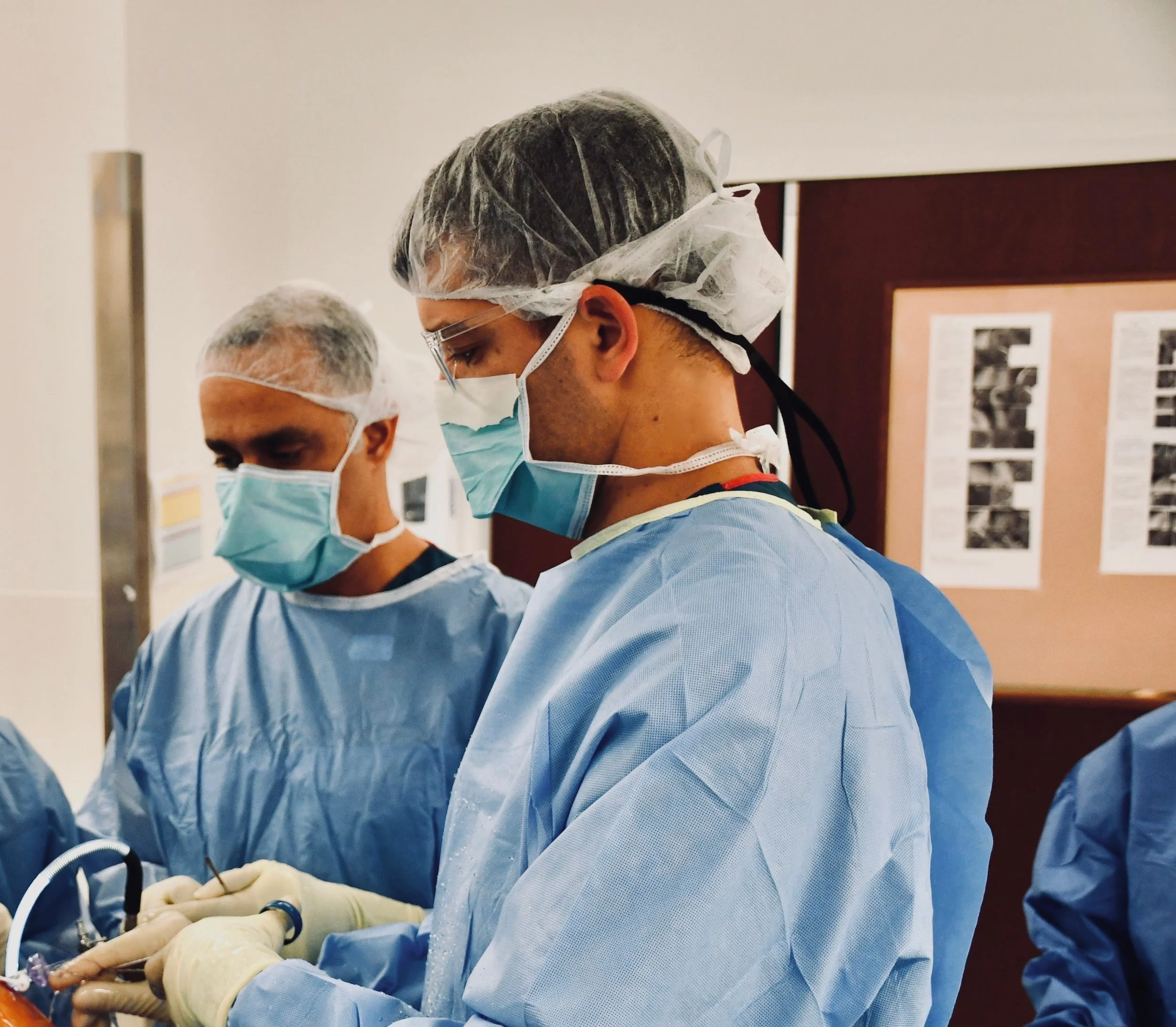 Medical professionals in scrubs, masks, and hair covers working together in a hospital or clinical setting.