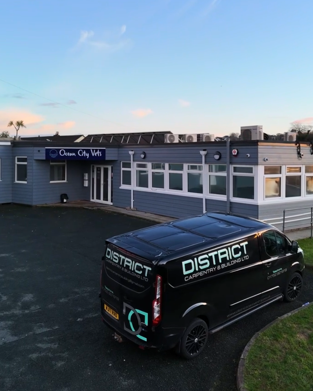 A commercial building with a sign labeled 'Ocean City Vets' and a black van with 'District Carpentry & Building Ltd' written on it parked in front.