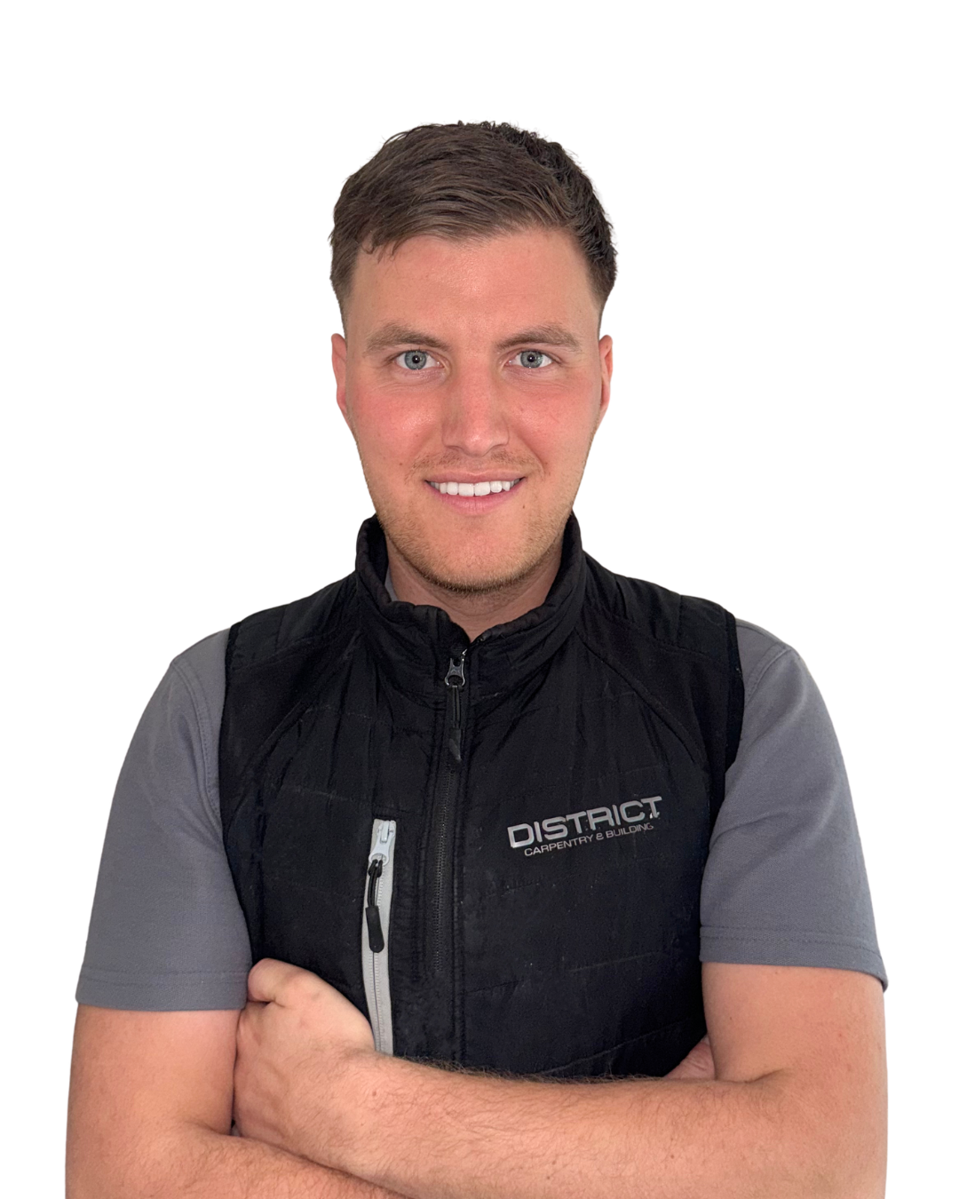 Portrait of a young man with short brown hair and blue eyes, smiling, wearing a black vest over a gray short-sleeved shirt, standing against a white background.