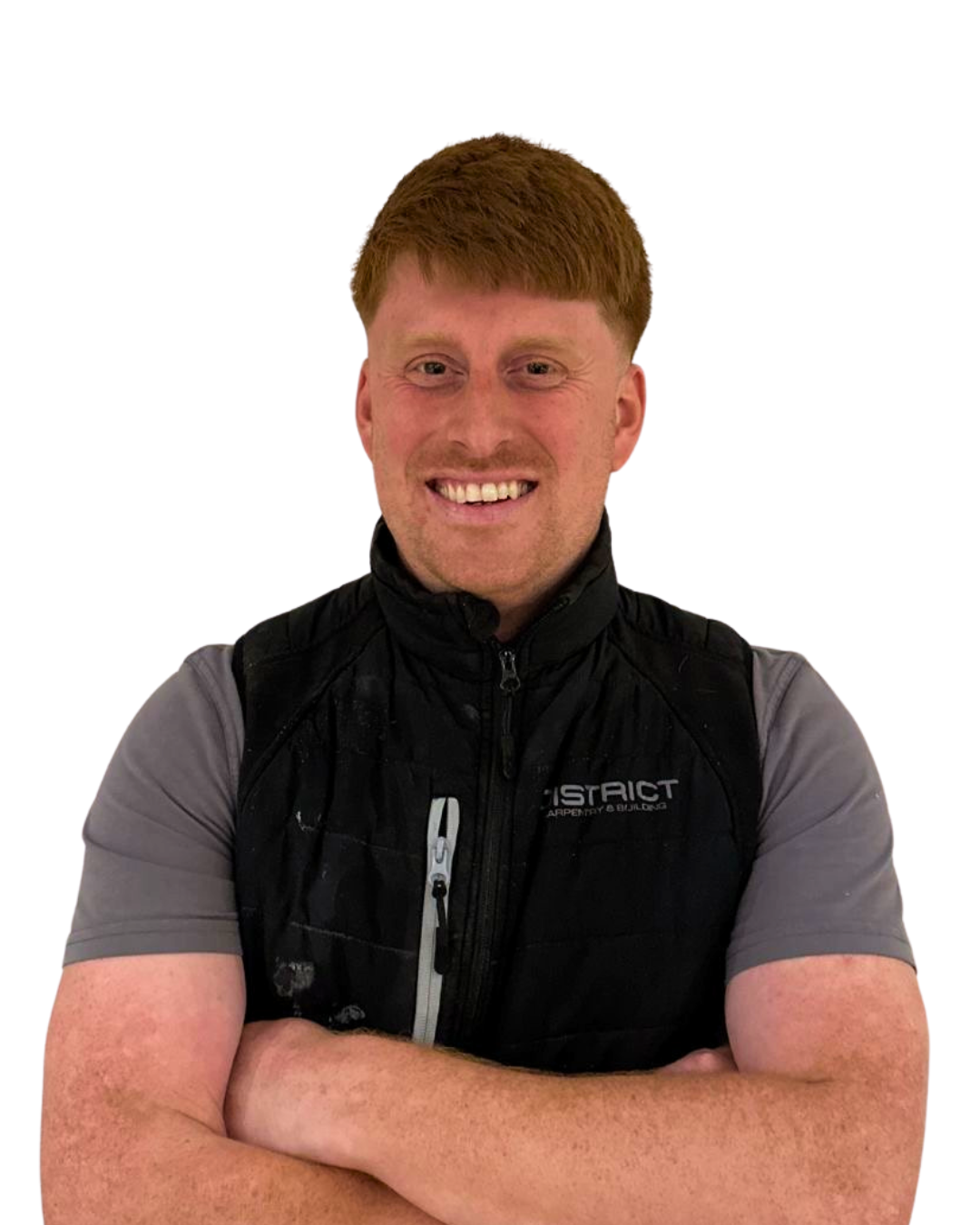 A smiling man with red hair, wearing a black vest over a gray t-shirt, crossing arms against a white background.