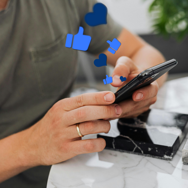 Person holding a smartphone with floating blue thumbs-up and heart icons.