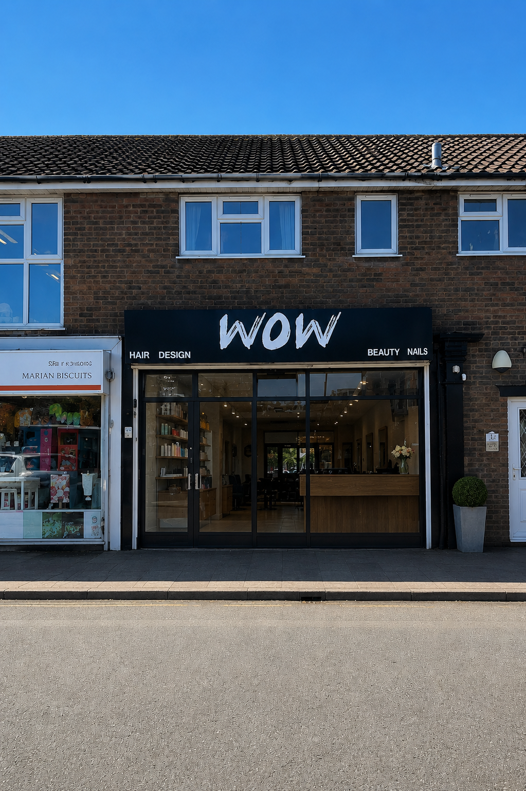 The WOW Storefront in  Codsall with a black sign that reads "WOW" and offers hair, design, beauty, and nails services, located between a gift shop and a sidewalk in a brick building with a tiled roof.