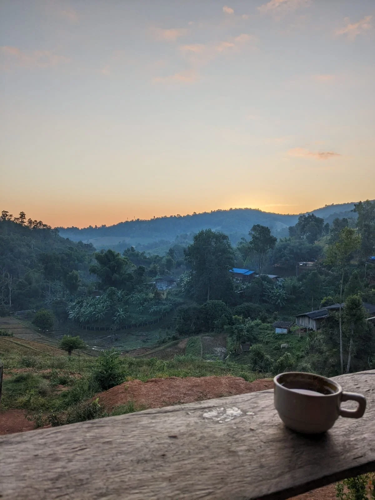 Eine Tasse Kaffee mit Blick auf den Sonnenaufgang mit einer Landschaft in der Natur und einem kleinen Karen-Bergdorf