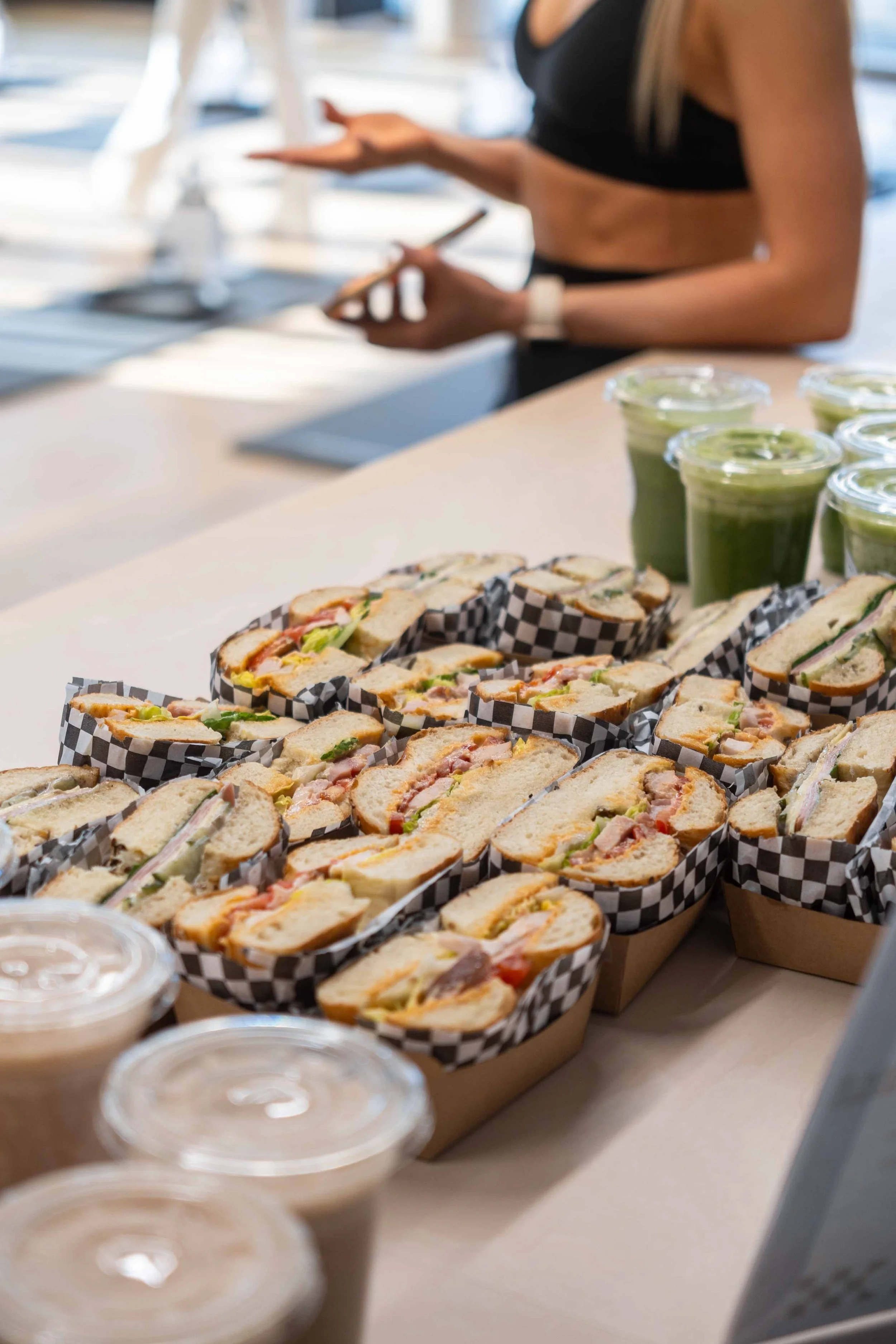 Assorted sandwiches and green smoothies on a table, with a person in athletic clothing in the background.