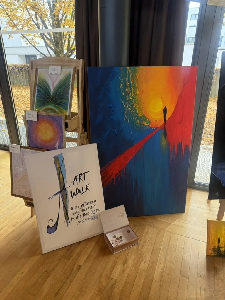 Eine Galerie mit bunten Gemälden, darunter ein großes abstraktes Bild mit einem roten Weg, einer Person und einem Sonnenuntergang, und ein Schild für eine Kunstwanderung, die das Einwerfen von Geld in eine Box für eine Karte anfordert.