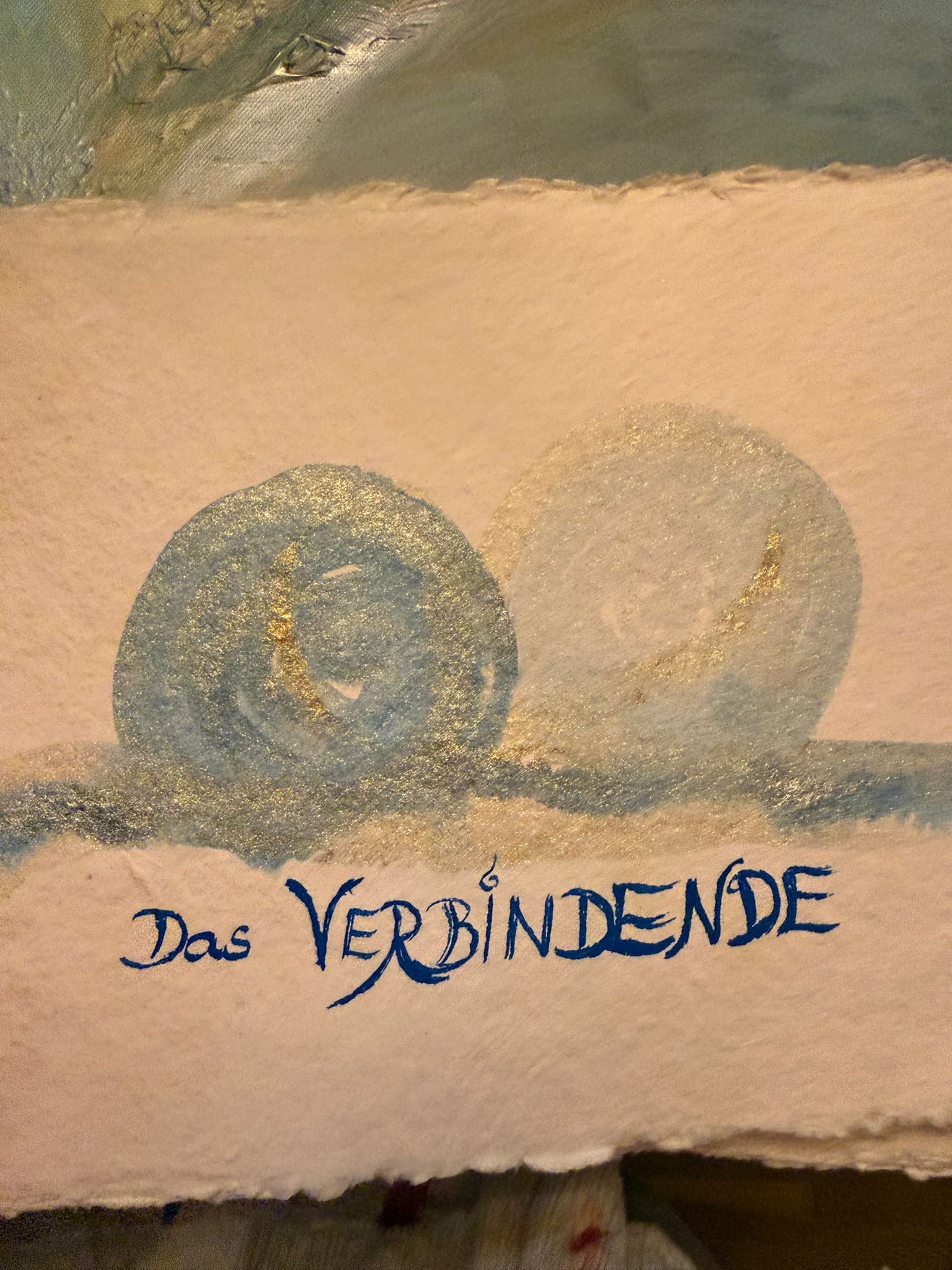 Handschriftlicher Text auf einer Karte mit goldenen Kreisen, darunter in blauer Tinte geschrieben: "Das VERBINDENDE" von der Anima Mundi Gründerin Anja Dreier gemalt.