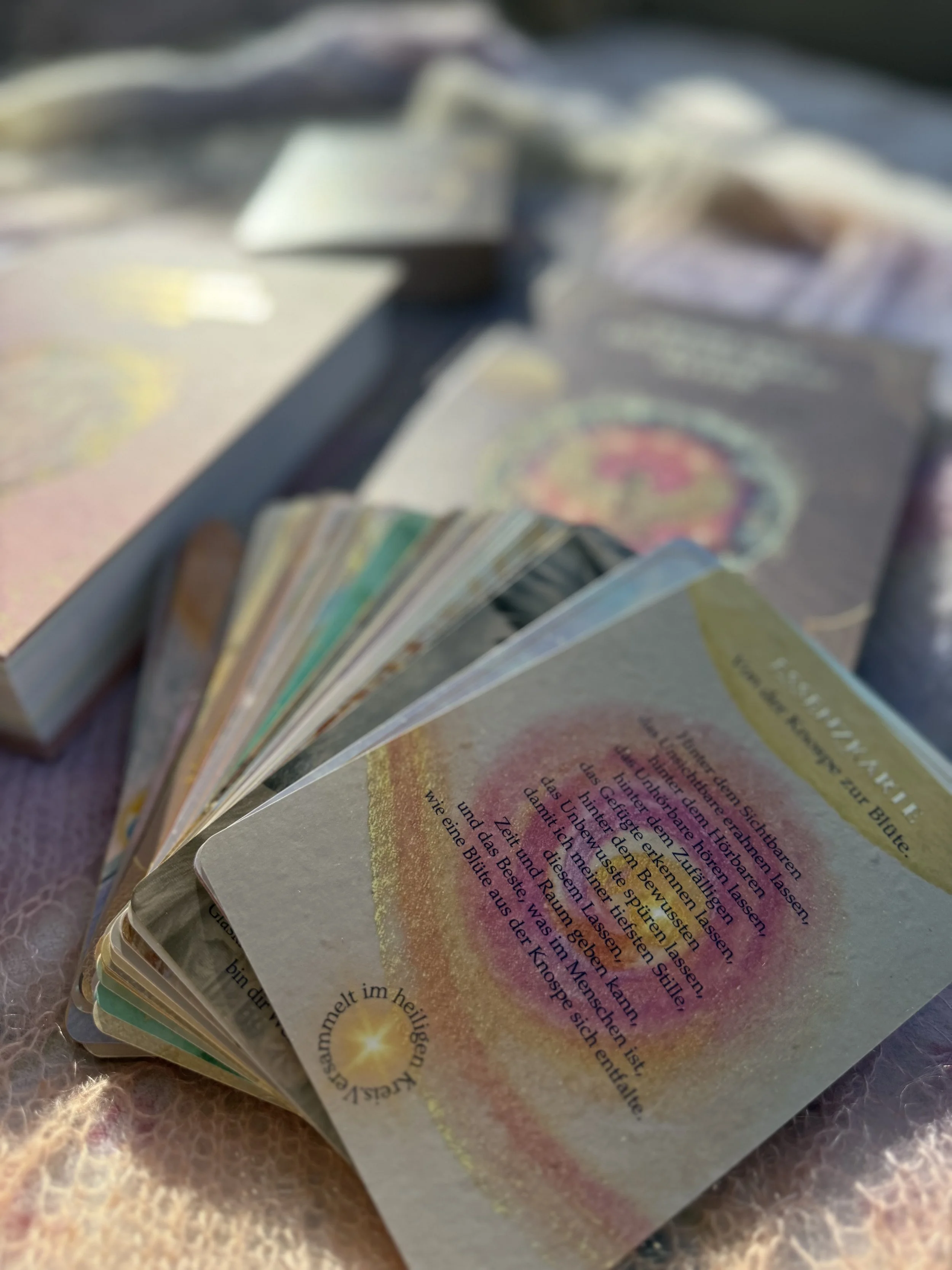 Aufgeklapptes Karteset mit einem bunten Kreisen-Design und Text, spirituelle Karte, auf einer weichen, flauschigen Oberfläche.