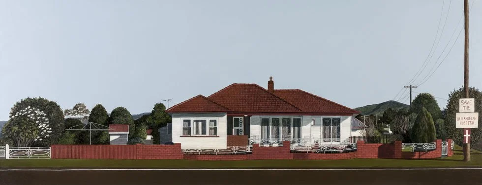 A white house with a red roof and red brick walls, surrounded by a red brick fence and greenery, with a sign reading 'Save the Bimbedah Hospital' near a power pole.