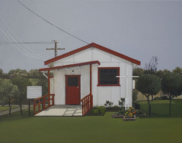 A small white building with a red roof and trim, surrounded by green grass and trees, and a flower bed in front.