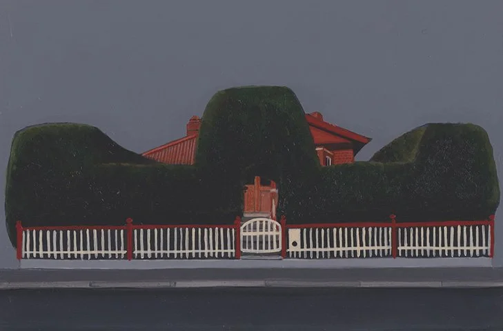 A house with a red roof surrounded by tall, rounded, well-trimmed hedges, and a white picket fence in front.