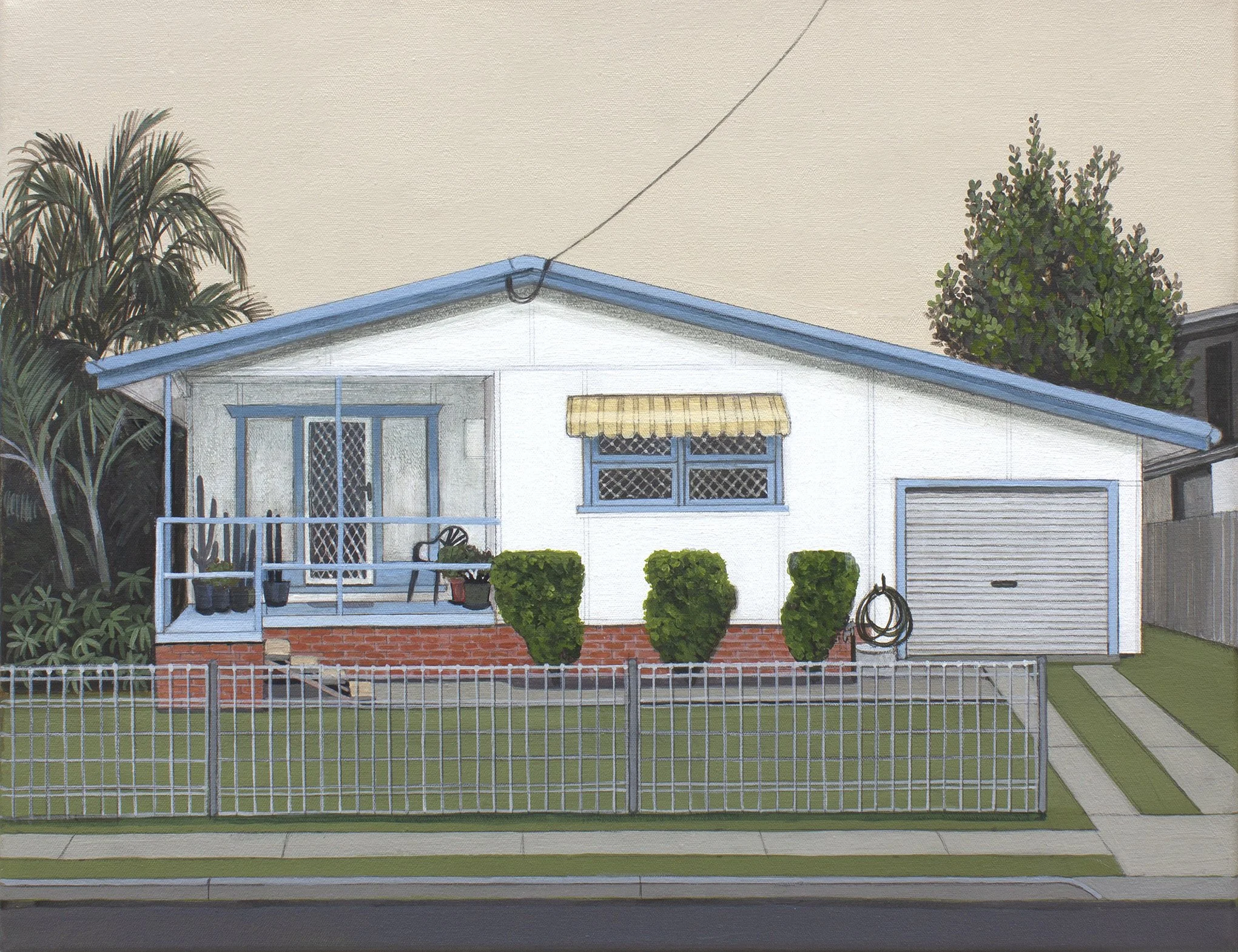 A house with a blue roof, a front porch, and two large bushes in front, surrounded by a white picket fence.