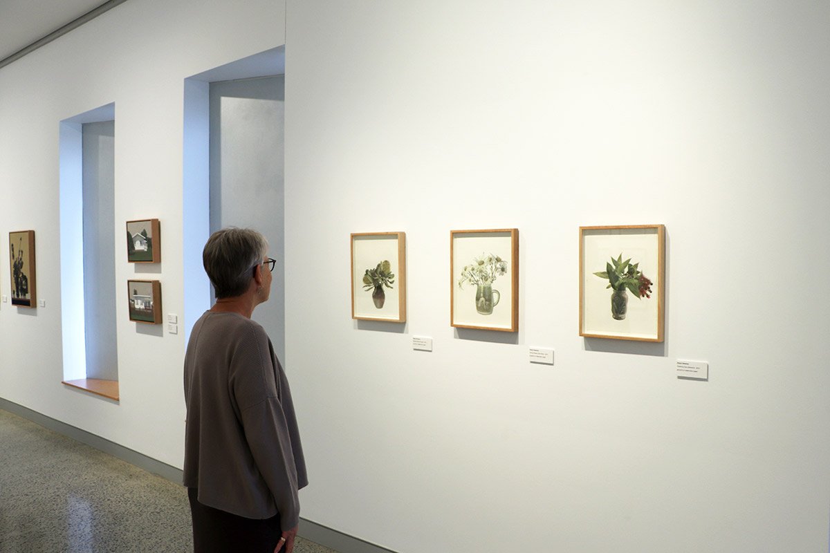 Person viewing framed botanical artwork of potted plants in an art gallery.