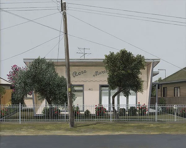 Small building with a white fence, two trees, and pink flowers in front.