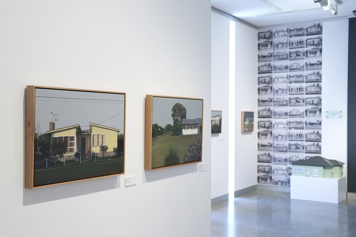 Gallery featuring paintings and photographs of houses and buildings, with a display of black-and-white images of architectural designs on one wall.