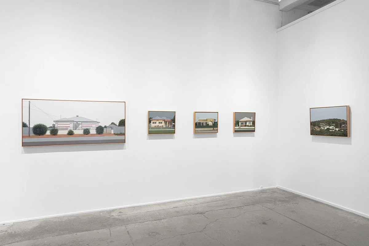 Gallery with five framed photographs of suburban houses on white walls.