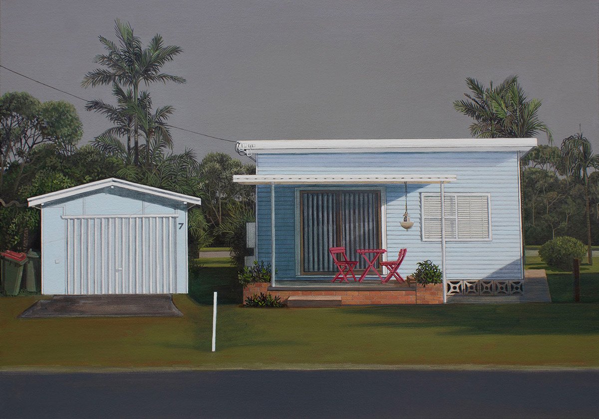 A light blue house with a small porch and a red table with two chairs, in front of a tree-lined area, next to a small white shed, under a cloudy sky.