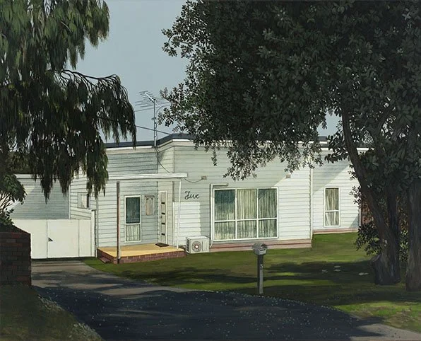 A white two-story house with a front porch, surrounded by trees, with a mailbox and a driveway.