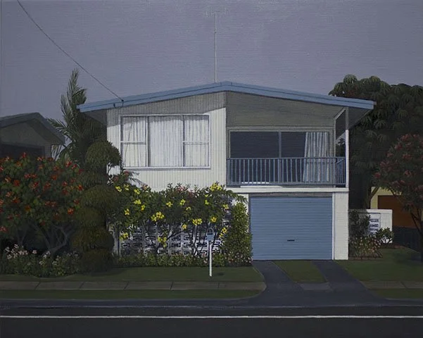 A two-story house with a garage, balcony, white exterior, and large front windows, surrounded by bushes and trees.