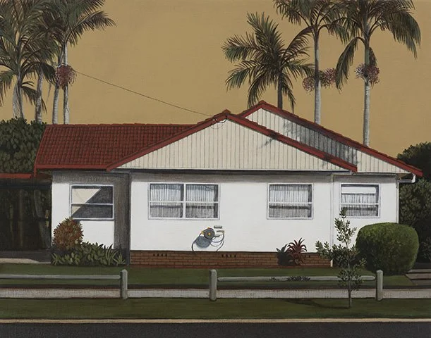 A white house with a red roof, decorated with a mural of a bird sitting on a branch on its front wall, surrounded by shrubs and trees including tall palm trees in the background.