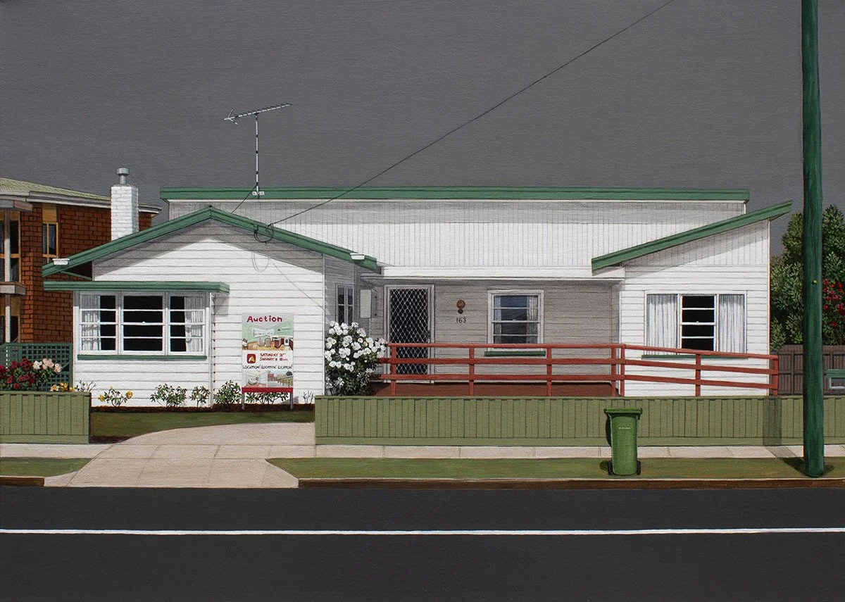 A white house with green roof accents and a red railing, front yard with flowers, sidewalk, and street, auction sign in yard.