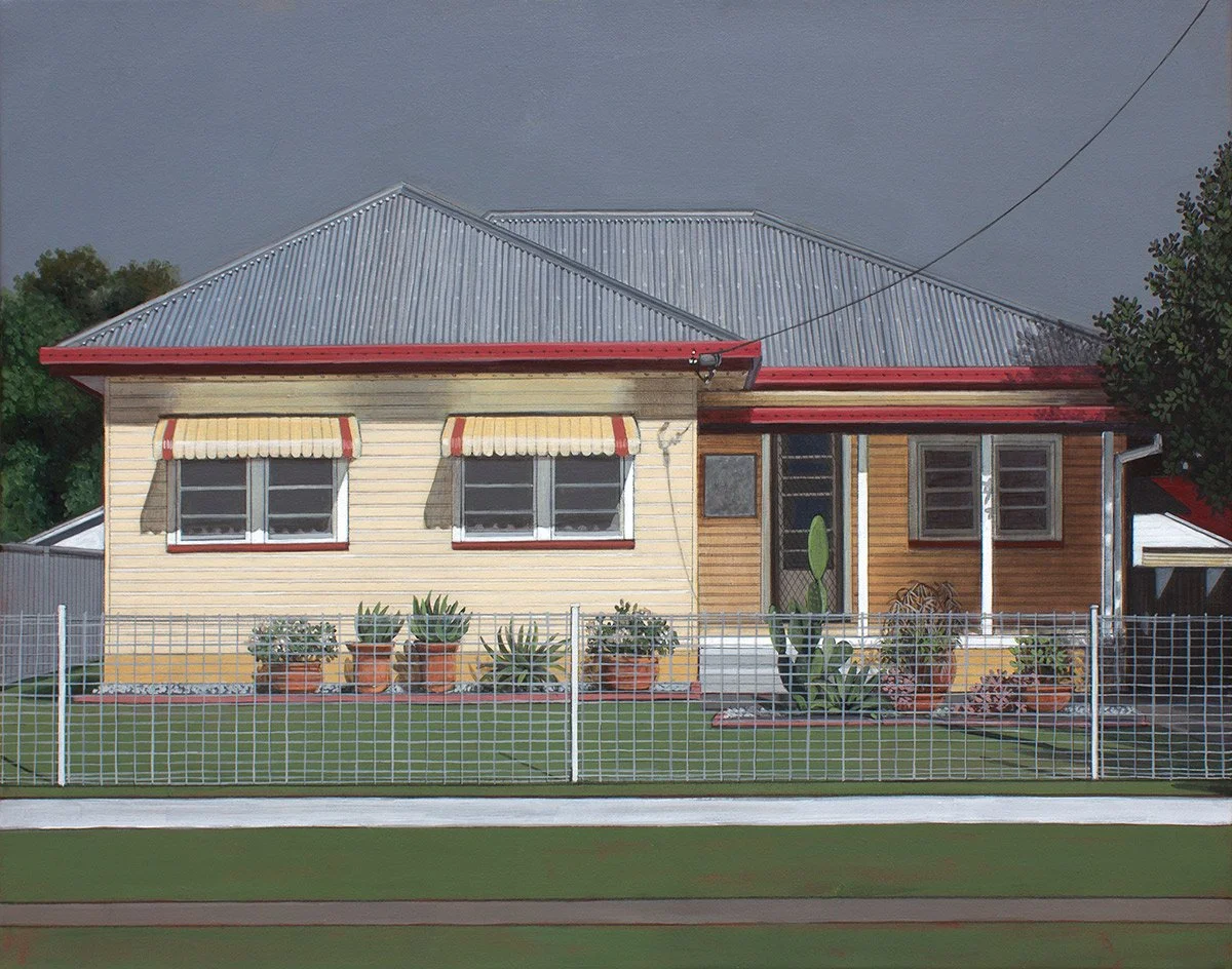 A single-story house with a gray metal roof, cream and wooden siding, front yard with potted plants, and a white fence.