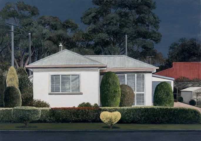 A white house with a metal roof, surrounded by neatly trimmed shrubs and trees, with a dark sky in the background.